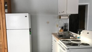 Una cocina funcional con muebles blancos, estufa integrada y refrigerador.