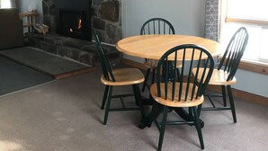 Una sala de estar acogedora con una chimenea de piedra, una mesa redonda de madera y cuatro sillas, además de un ventilador de techo.