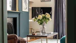 Un salon avec une cheminée, un téléviseur, un vase de fleurs et un lustre.