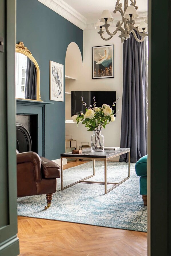 A living room with a fireplace, a television, a vase with flowers, and a chandelier. - Elegant Bath Apartment Near Royal Crescent (Bath)
