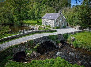A stone bridge over a stream leading to a stone house with a garden and picnic table. - Otter Cottage - sleeps 6 guests  in 3 bedrooms (Pwllheli)