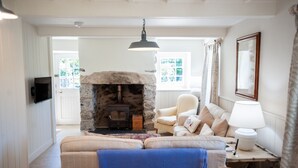 A cozy living room with a stone fireplace, a comfortable sofa, a blue chair, and a table with a lamp. - Otter Cottage - sleeps 6 guests in 3 bedrooms (Pwllheli)