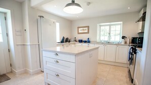 A modern kitchen with white cabinetry, a large island with drawers, a Bosch refrigerator, and a window providing natural light. - Otter Cottage - sleeps 6 guests in 3 bedrooms (Pwllheli)