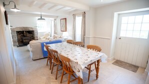 A dining area with a table set for six, wooden chairs, a stone fireplace, and a cozy seating area with a sofa and armchairs. - Otter Cottage - sleeps 6 guests in 3 bedrooms (Pwllheli)