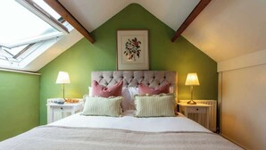 Ein Schlafzimmer mit grüner Wand, einem gepolsterten Kopfteil, zwei Nachttischen mit Lampen und einem Oberlicht.