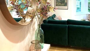 A living room with a green sofa, a round mirror, and a vase with dried plants. - Elegant Apartment | Balcony & Free Parking (Bath)