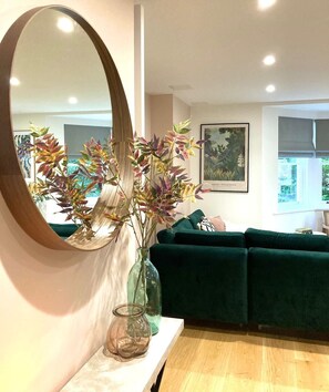 Relax in this stylish living room with a green sofa, framed botanical illustration, and elegant glass vase.