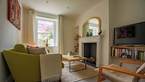 Una sala de estar con sofá, sillón, chimenea, televisor y estantería.