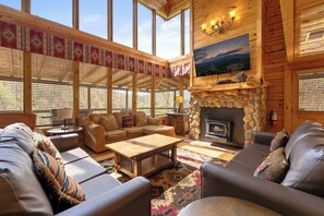 A cozy log cabin interior with a fireplace, leather sofas, and large windows. - Mountainside Stay for 12 w/Hot Tub & Mtn Views (Sevierville)