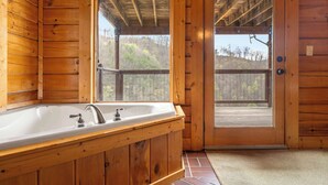 Ein Badezimmer einer Holzhütte mit einer großen Badewanne, Holzwänden und Blick durch eine Glastür.