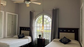 Een slaapkamer met twee bedden, een plafondventilator, een raam met gordijnen en een kledingkast.
