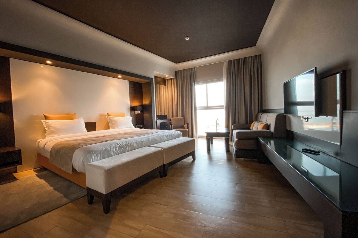 A modern hotel room with a large bed, a seating area, a television, and a large window.