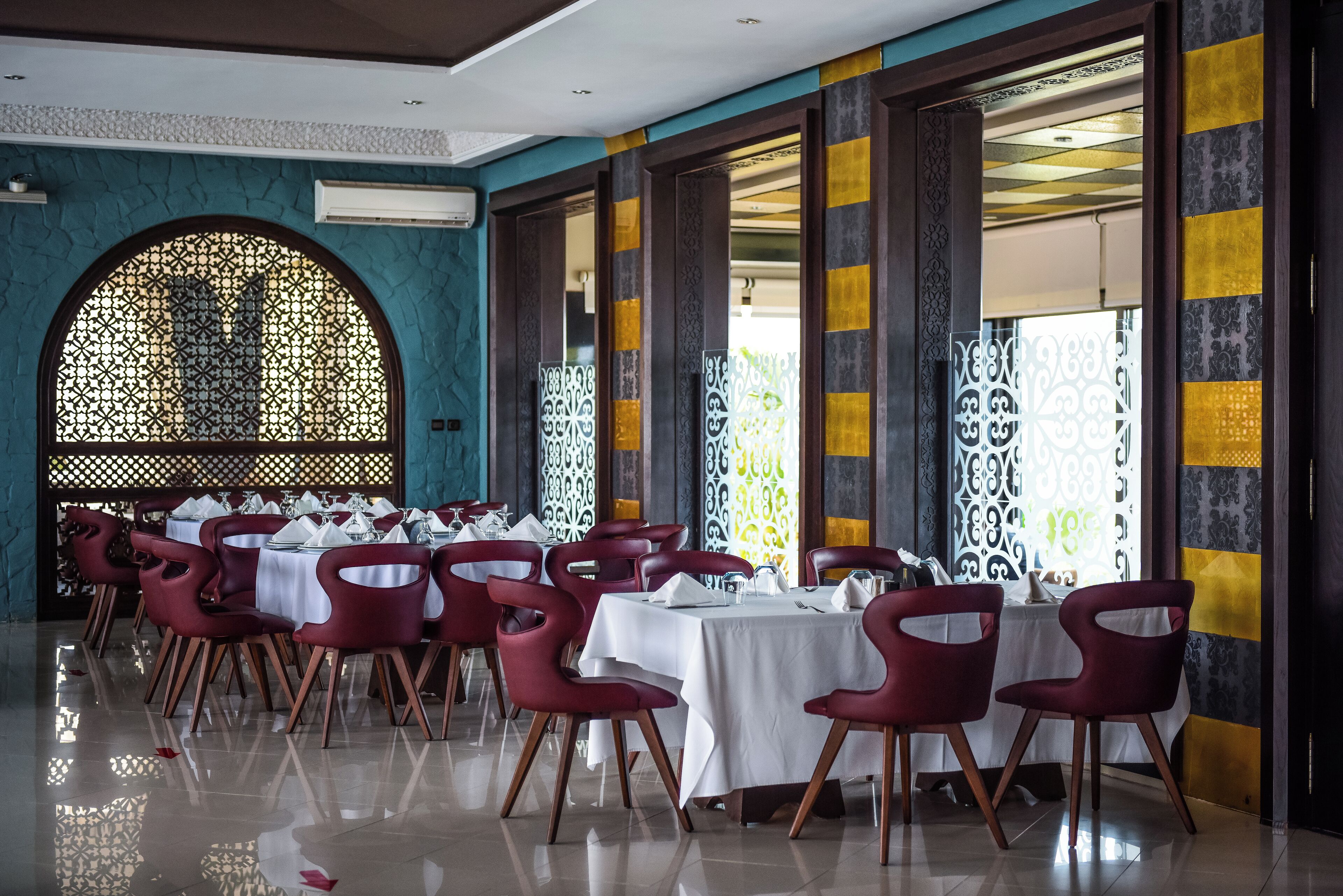 A dining area with tables set for multiple guests, featuring red chairs and white tablecloths.