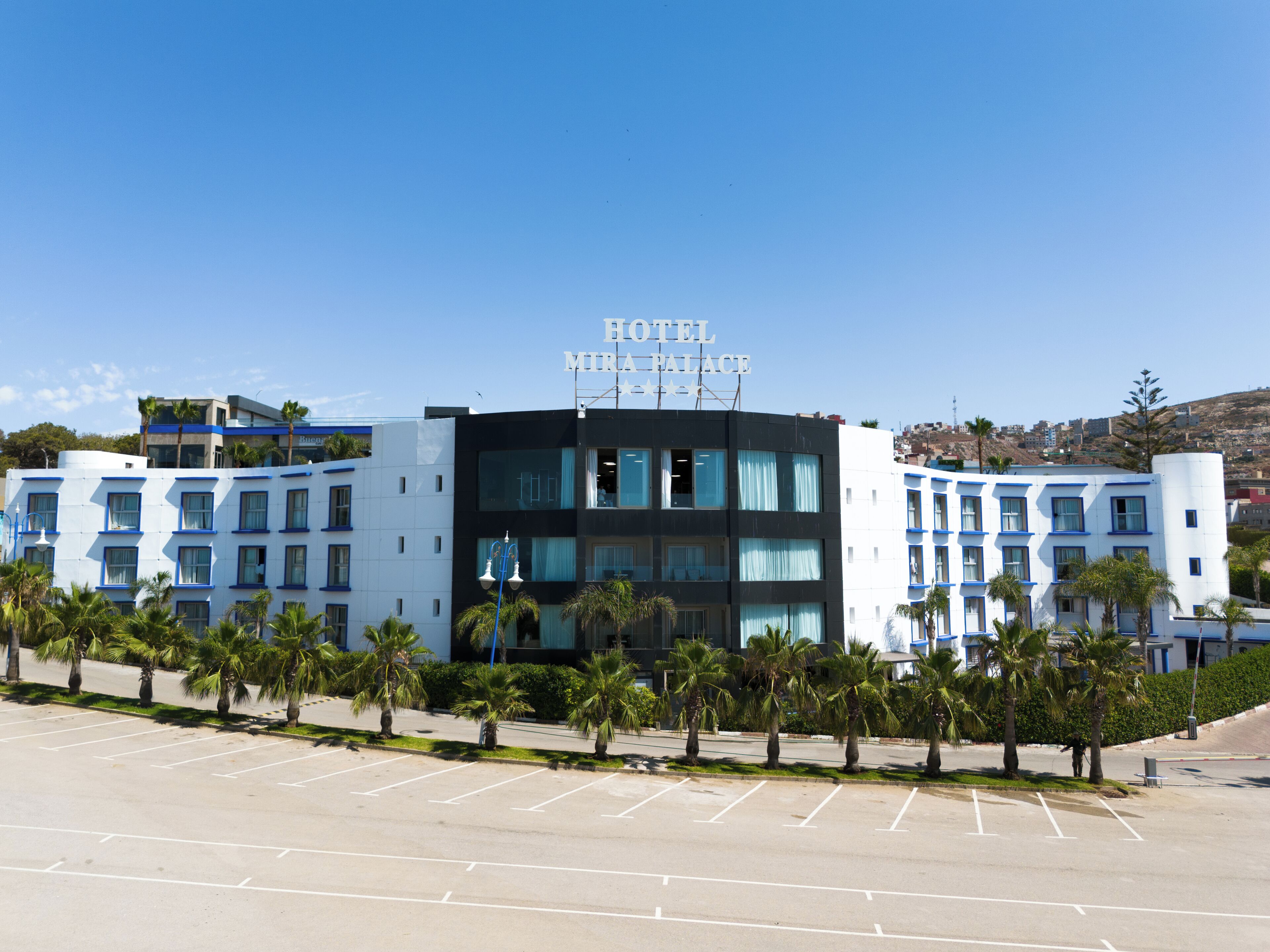A hotel with a modern facade, multiple floors, and a parking lot in front.