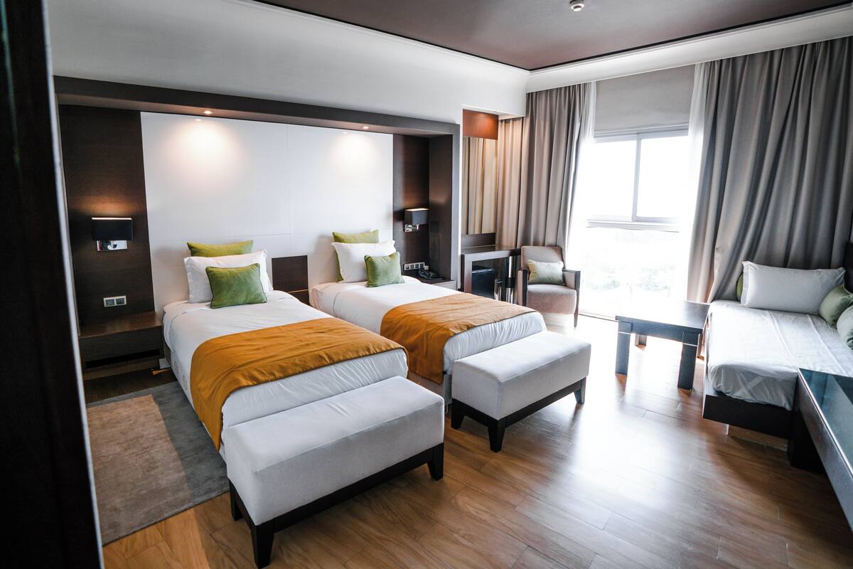 A hotel room with two beds, a desk, a chair, and a large window.