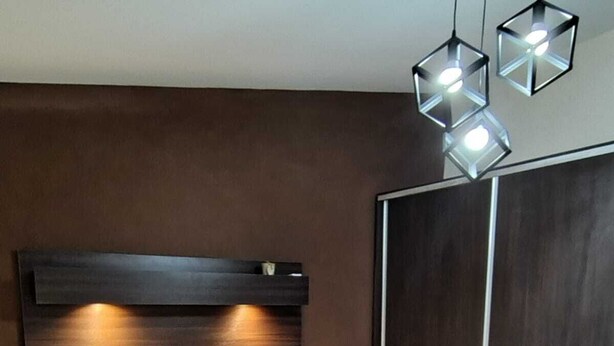 Un lit bien fait, avec une couette blanche et des oreillers, une tête de lit en bois et une paire de lampes suspendues aux formes géométriques.