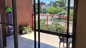 Un balcon donnant sur un paysage urbain, une structure métallique rouge et une chaise.