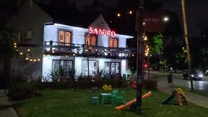 Un bâtiment orné d’une enseigne au néon sur laquelle on peut lire « SANDRO », et d’un balcon décoré de guirlandes lumineuses.