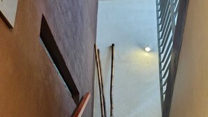Un escalier recouvert de carreaux beiges, une main courante en bois et un pot noir contenant des tiges de bambou.