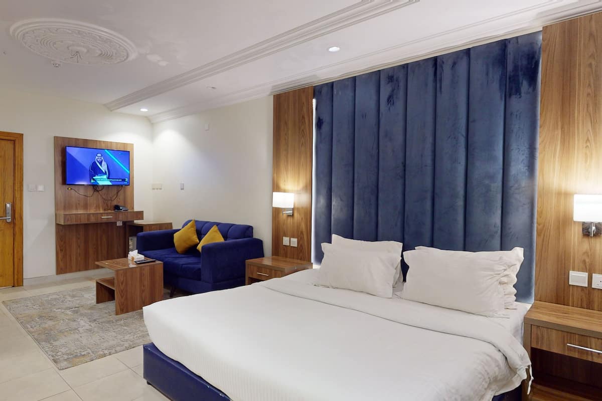 Habitación de hotel con una cama grande, un sofá azul, un televisor montado en la pared y una puerta de madera.