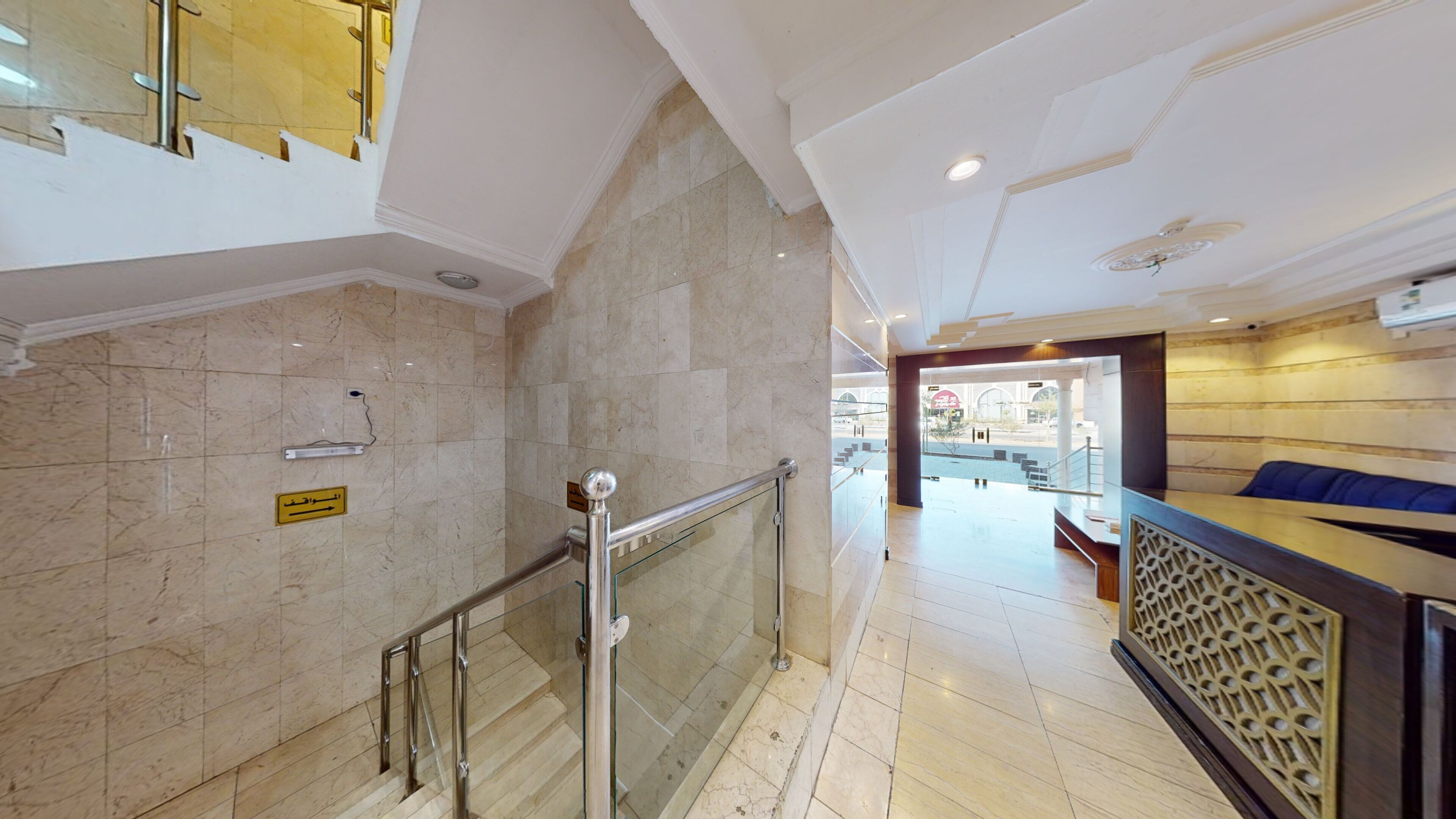 Een moderne hotellobby met marmeren vloer, een glazen balustrade en een receptiebalie met decoratieve scheiding.