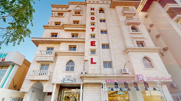 Ein Hotel mit einem gut sichtbaren „HOTEL“-Schild, mehreren Balkonen und einer Schaufensterfront mit der Aufschrift „ROSE SWEETS“.