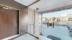Entrada con puerta de madera, escalera metálica y vista a una calle con un McDonald’s y un cartel.