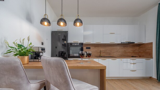 Una cocina moderna con armarios blancos, encimera de madera y dos lámparas colgantes.