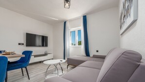 Una sala de estar moderna con un sofá, una mesa de comedor con sillas, un televisor de pantalla plana y una ventana con cortinas.