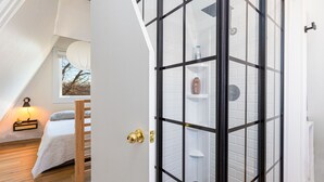 A bedroom with a sloped ceiling, a bed, a bedside table with a lamp, and a window with a view of trees. - 🏠 Mid-Century A-Frame Near Galena | Stargaze | Couples Retreat | 1 Bed/1 Bath (Elizabeth)
