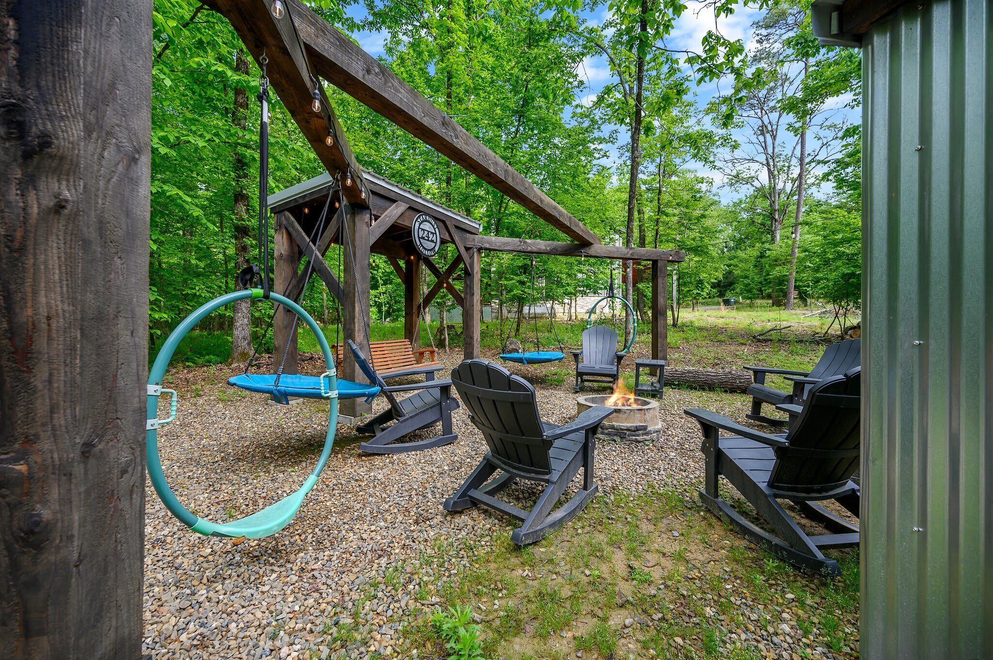 A wooden deck with Adirondack chairs, a swing set, and a fire pit.