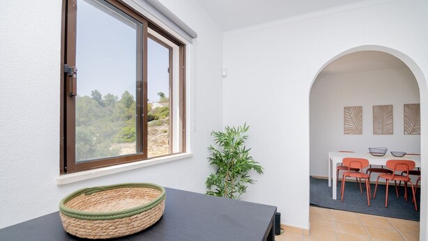 A room with a large window, a woven basket on a table, a plant, and a dining area with chairs and a table. - Centeanes beach II by Innkeeper (Carvoeiro)