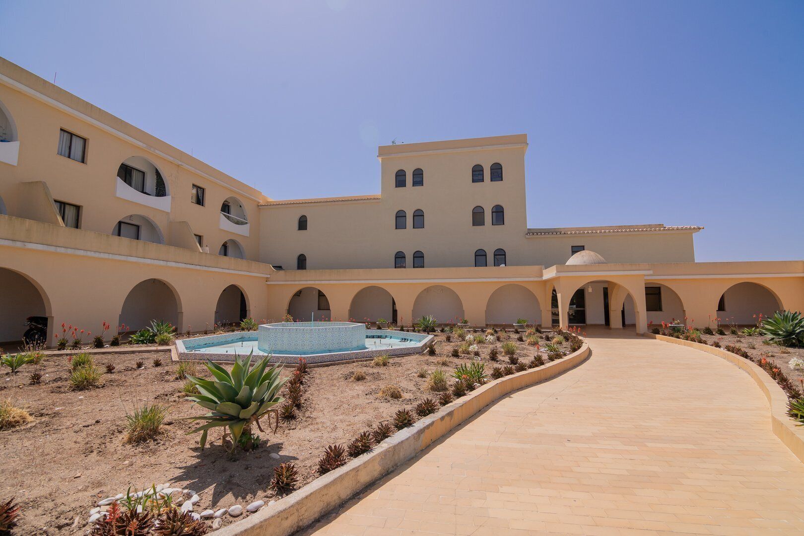 A courtyard with a pool, surrounded by arches and a central walkway.