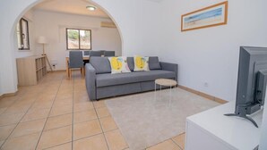 A living room with a grey sofa, a small round table, and a television. There is a dining area in the background with a table and chairs. - Carvoeiro sea view (Carvoeiro)