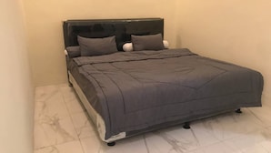 A single bed with a dark headboard and grey bedding in a room with white walls and a tiled floor. - Hotel O Griya Mbah Rono (Yogyakarta)