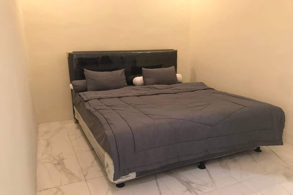 A single bed with a dark headboard and grey bedding in a room with white walls and a tiled floor.