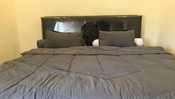 A bed with a dark grey quilt and two pillows, a black headboard, and a white bedside table. - Hotel O Griya Mbah Rono (Yogyakarta)