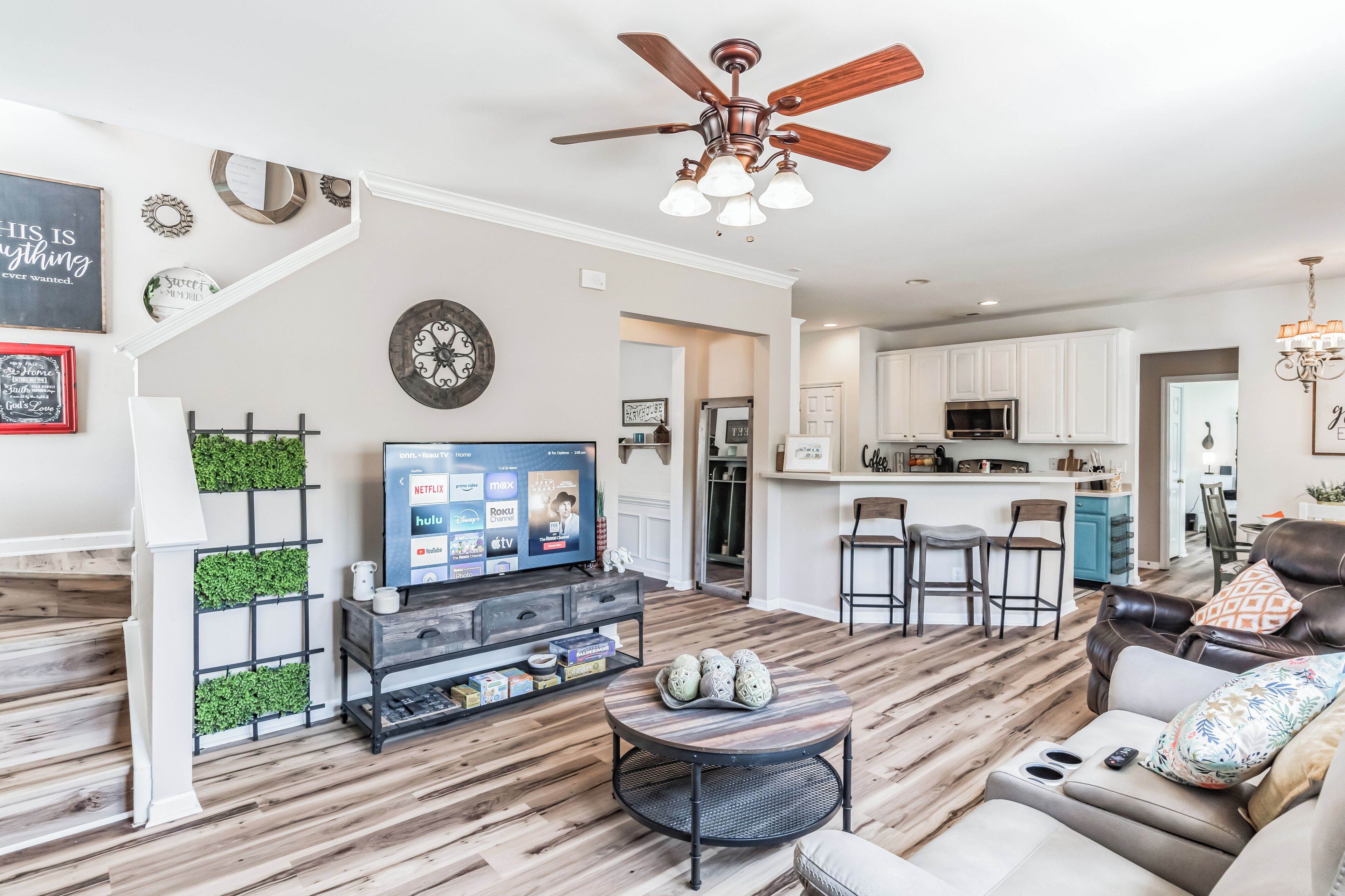 A modern living room with a TV, seating, and a kitchen in the background.