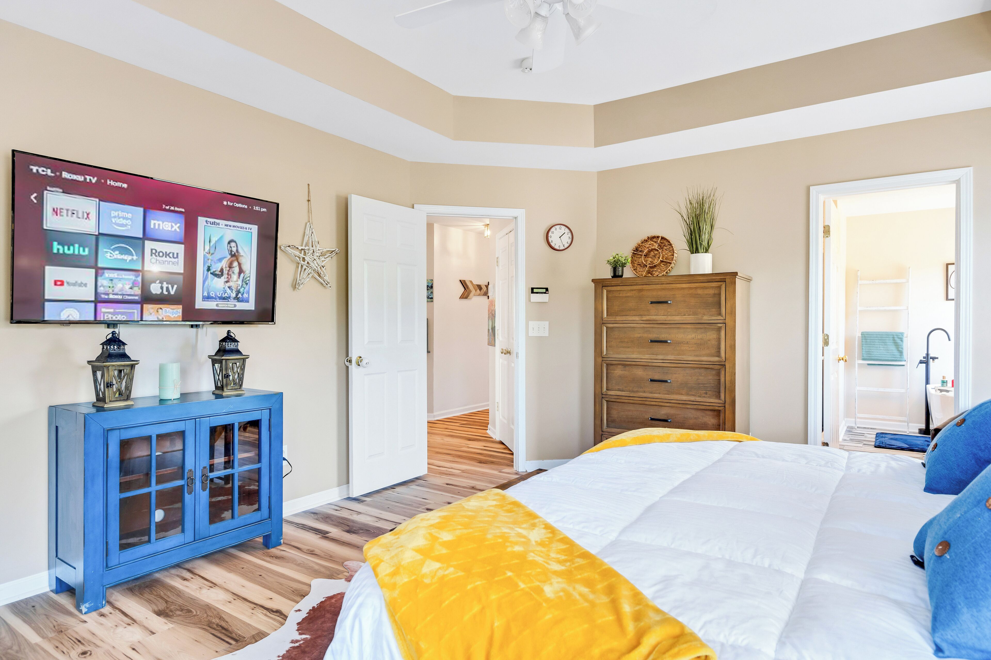 A bedroom with a bed, a TV on a blue cabinet, a wooden dresser, and a door leading to another room.