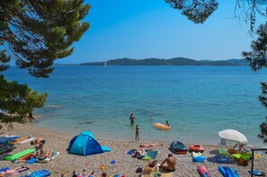Ein Strand mit klarem Wasser, badenden Personen und einem Zelt.
