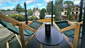 Une terrasse dotée de deux fauteuils verts rembourrés et d’une petite table ronde, offrant une vue sur un quartier résidentiel avec ses maisons et ses arbres.