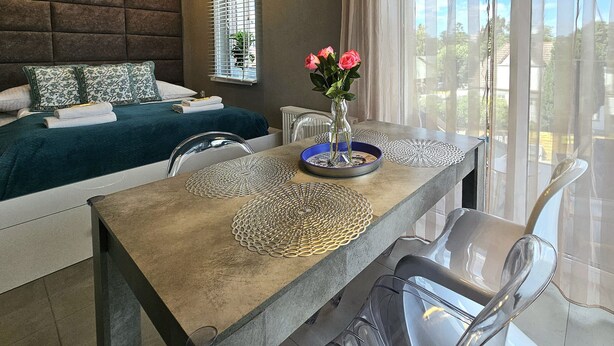 Une chambre d’hôtel avec un lit, une table à manger avec des sets de table, un vase avec des fleurs et une vue par la fenêtre.