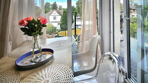 Une pièce avec une grande fenêtre, un vase rempli de fleurs, une chaise et une table sur laquelle est posée une assiette décorative.