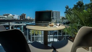 A laptop on a table with a glass of coffee, two chairs, and a view of buildings and trees. - Mediteranean Luxury Apartment (Chania)