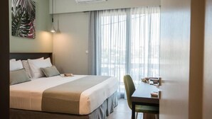 A hotel room with a bed, bedside table, chair, and a large window with curtains. - Mediteranean Luxury Apartment (Chania)