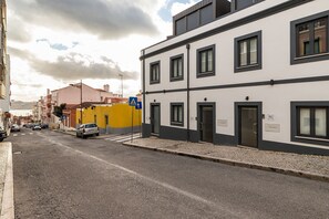 A street with buildings, a pedestrian crossing, and cars parked along the side.