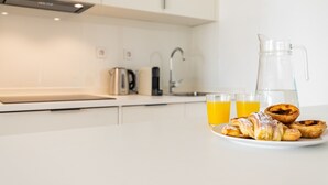 Una cocina con encimera blanca, una cafetera, una jarra y un plato de pasteles.