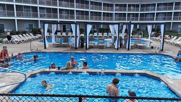 A swimming pool with lounge chairs and umbrellas, surrounded by a building with multiple balconies.