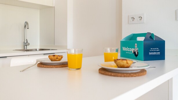 A kitchen counter with two plates of food and two glasses of orange juice, a blue tote bag, and a white wall with a power outlet. - Belem Design 08 by Homing (Lisbon)