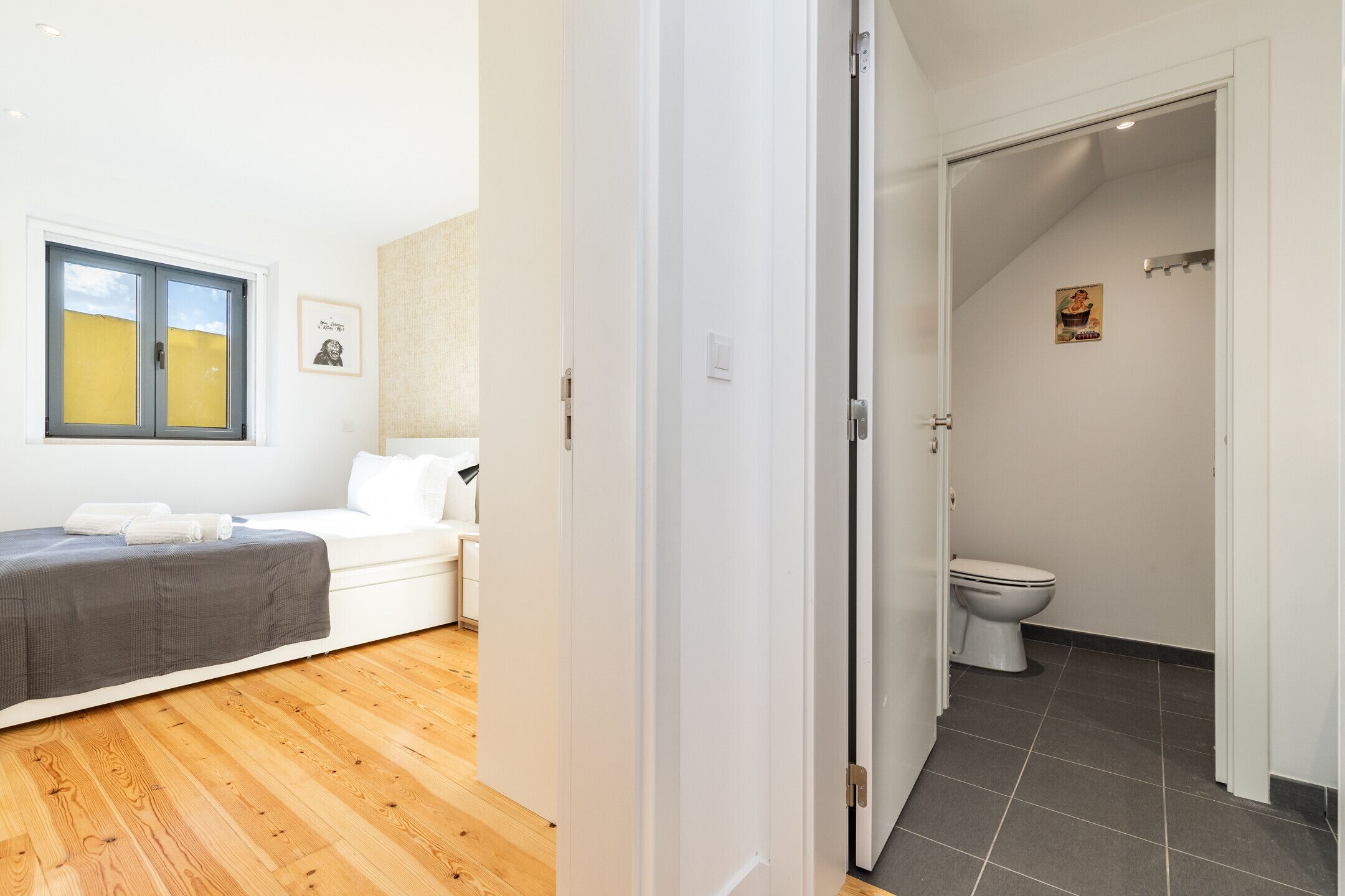 Ein modernes Schlafzimmer mit Holzboden, einem weißen Bett und einem Fenster mit Jalousien.